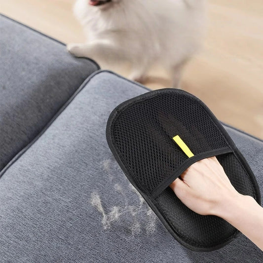 Person using a black pet grooming tool on a gray surface with a blurred dog in the background